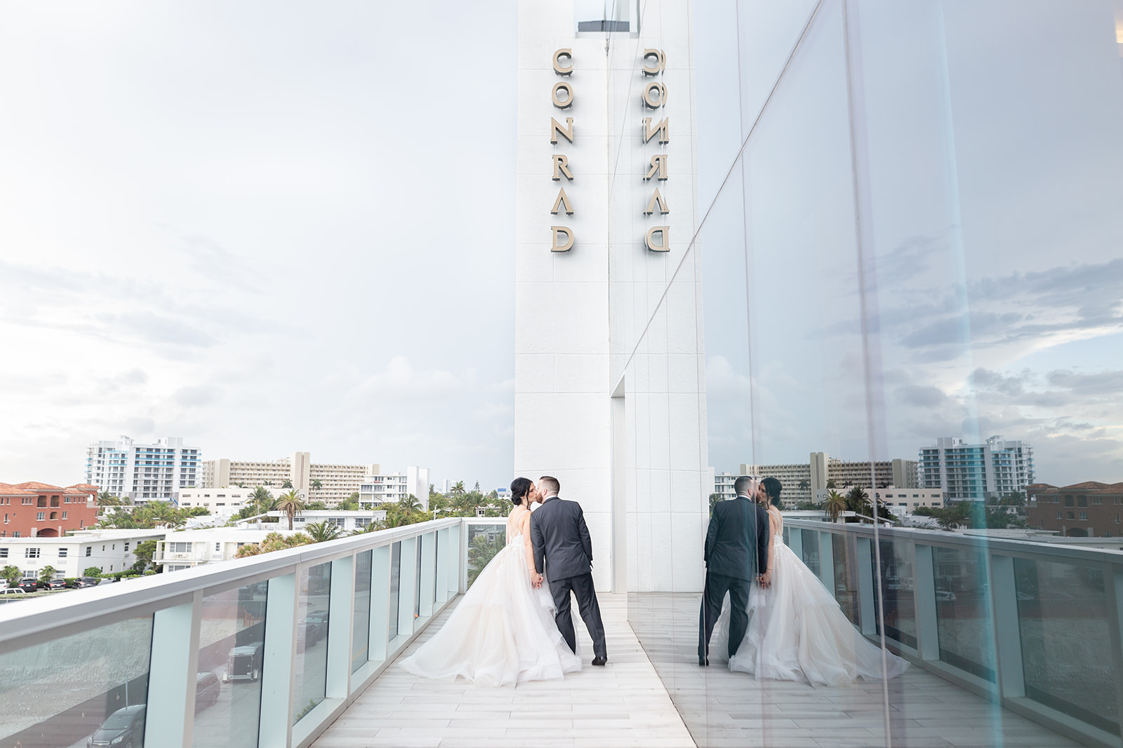 bride and groom kiss on the balcony of the Conrad Fort Lauderdale Beach with their reflection in the window
