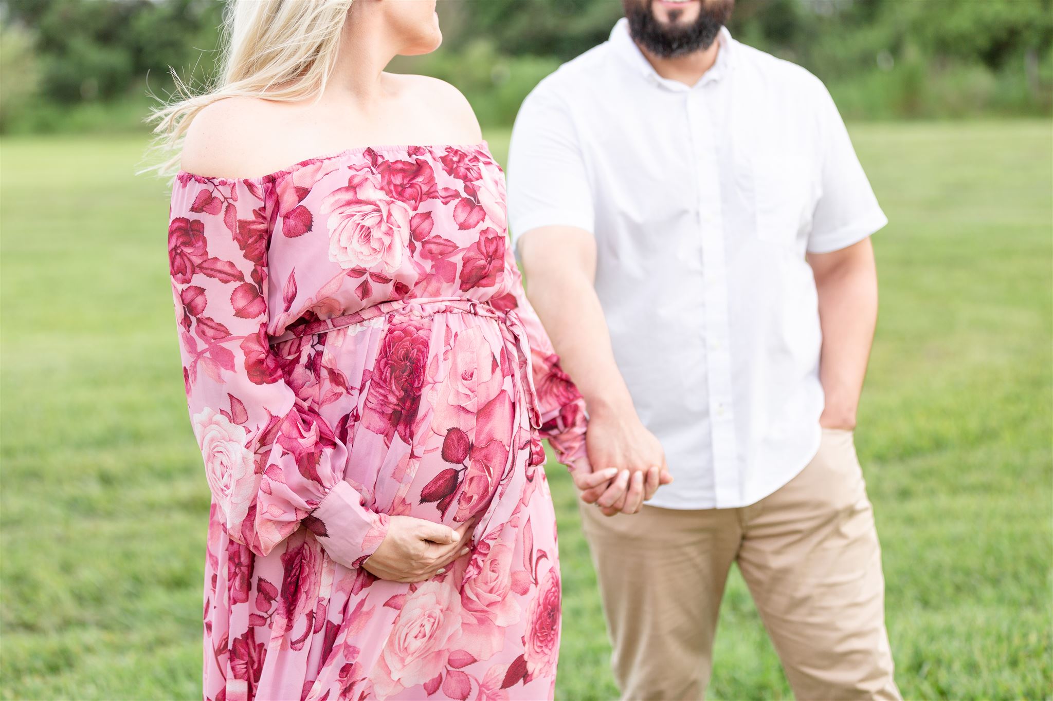 closeup of expecting mother in pink floral dress holding hands with her husband in Robbins Lodge maternity photos